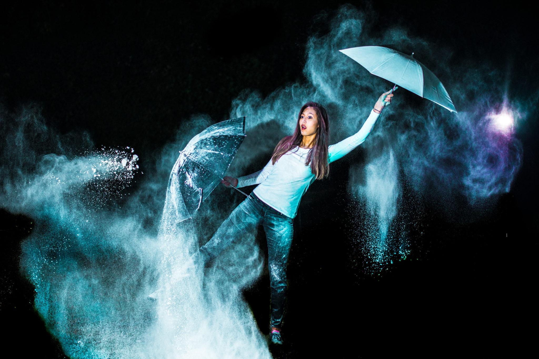 Student holding two umbrellas in colorful clouds on a dark background